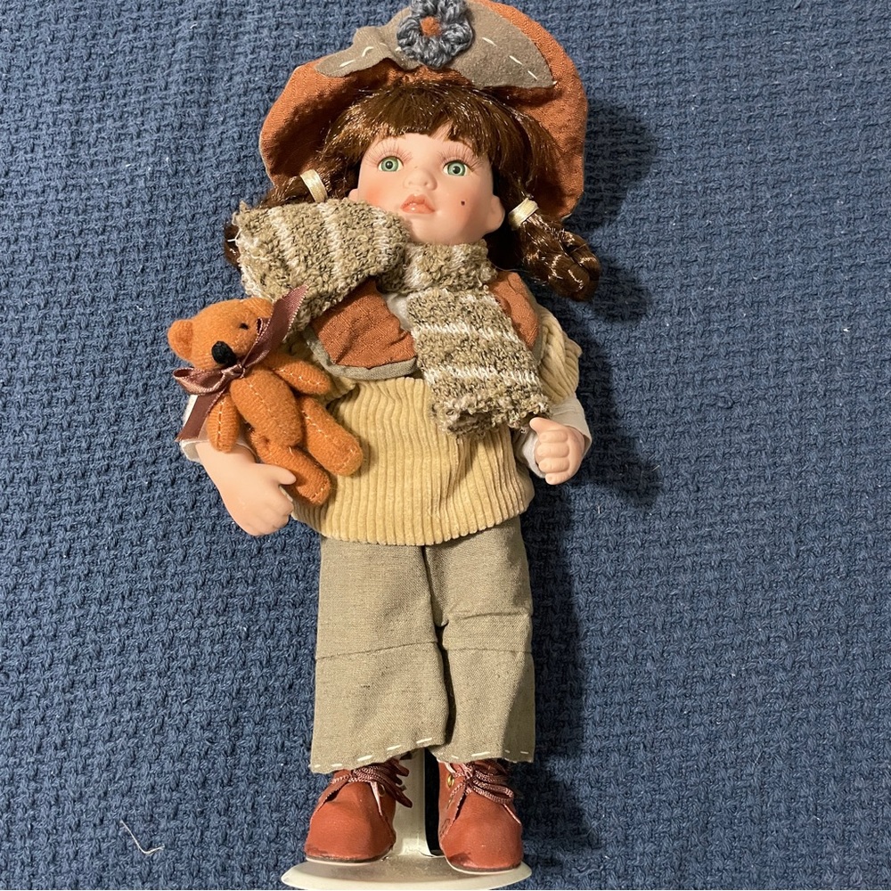 Small porcelain doll with teddy bear. Comes with display stand.